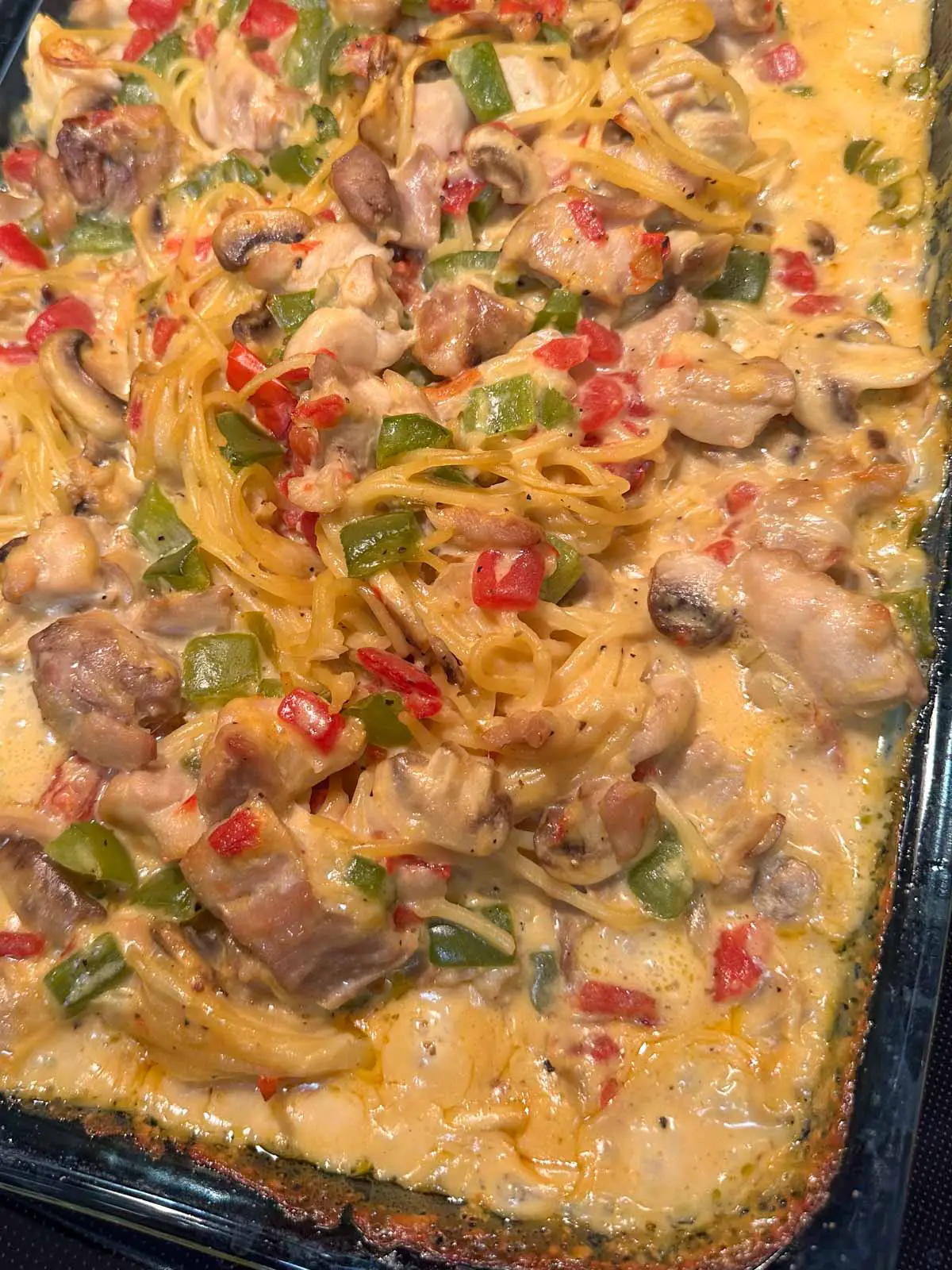 A glass casserole dish containing Texas Chicken Spaghetti which is spaghetti in a creamy sauce with tomatoes, mushrooms, chicken green chilies, and green bell peppers.