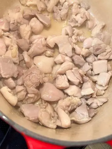 A red Dutch oven containing pieces of cooked chicken thighs.