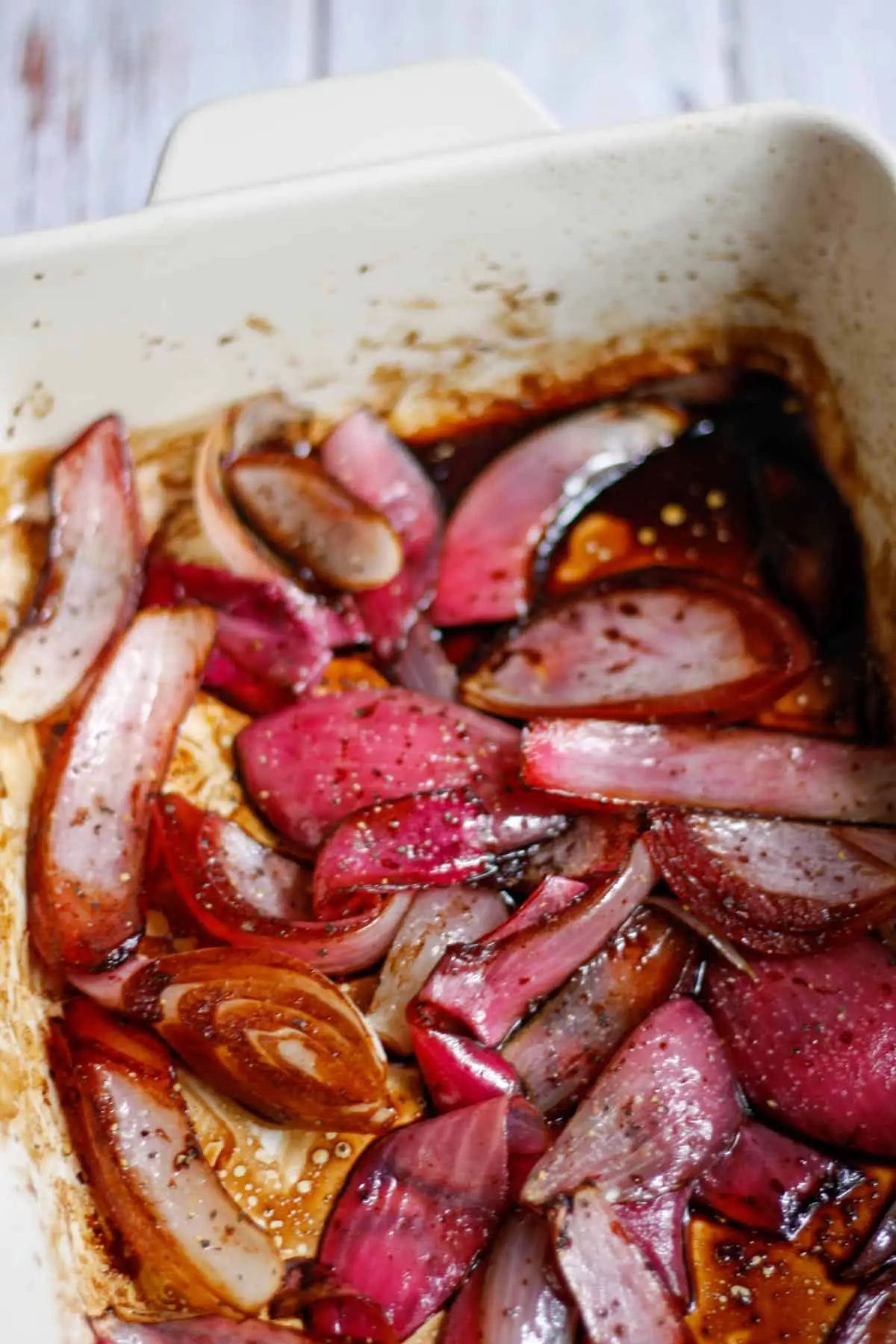 A casserole dish containing roasted red onions in balsamic vinegar and seasoned with salt and pepper.