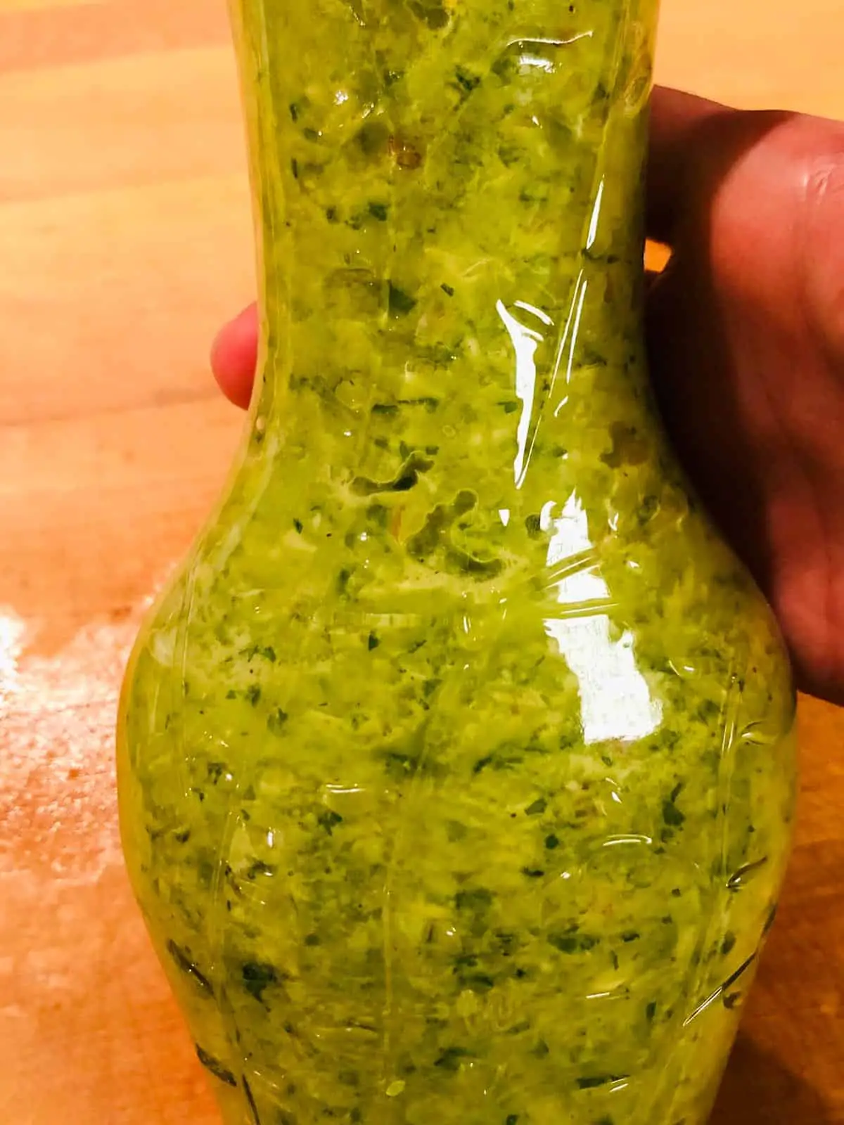 A glass bottle with green Haitian epis held by someone's hand.