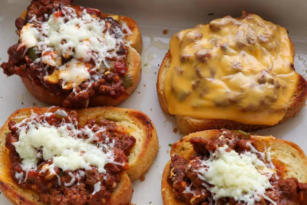A white dish containing pieces of Texas Toast topped with sloppy joe sauce. Several pieces are topped with melted cheddar and one has melted American cheese.