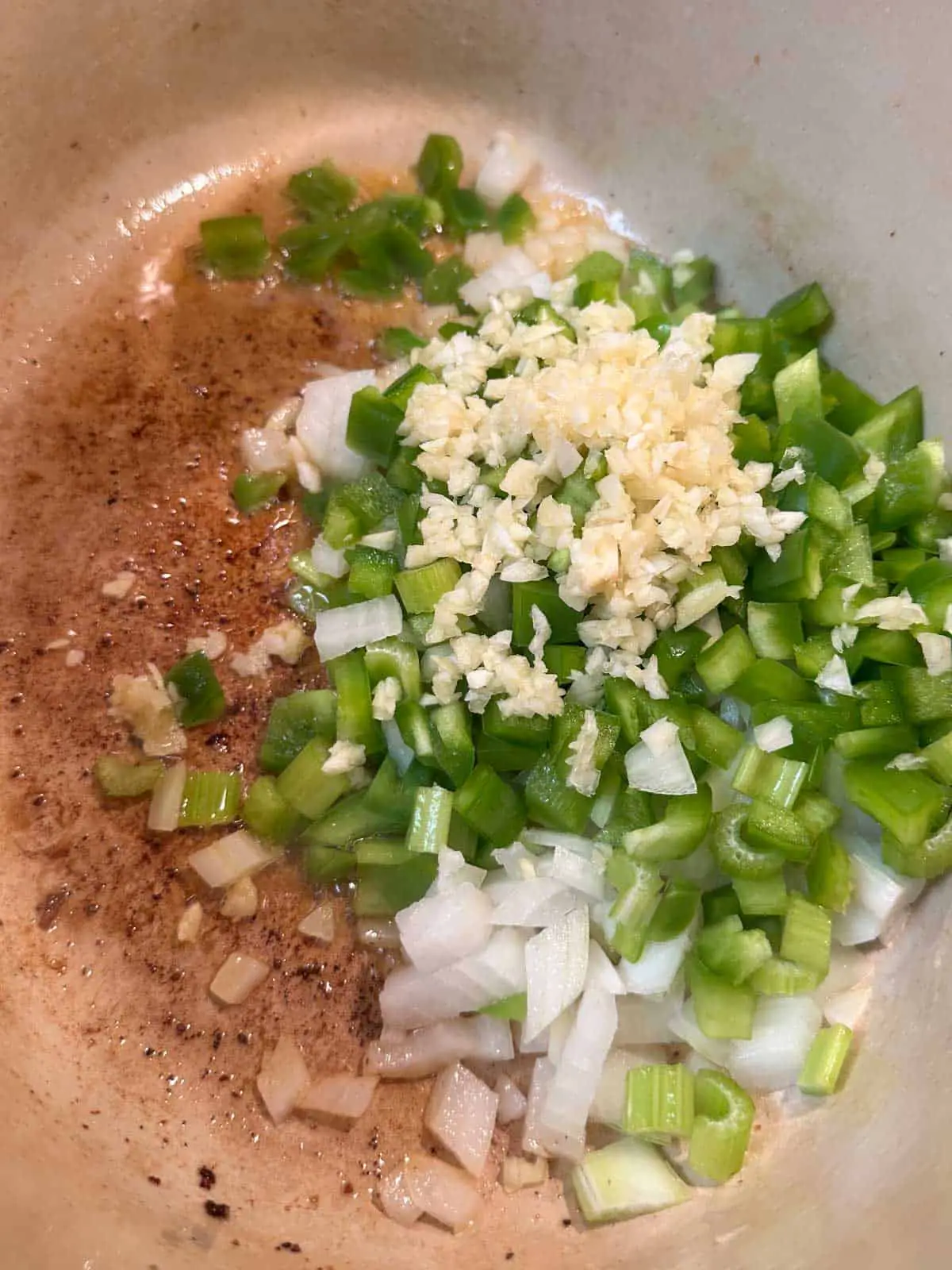 A red Dutch oven containing melted butter and diced celery, green bell peppers, onion, and minced garlic.