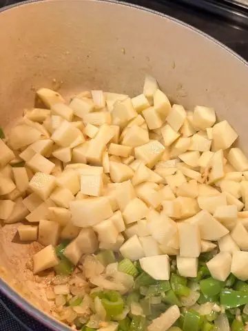 A Dutch oven containing bite sized pieces of potatoes and diced green bell peppers, celery, and onions.
