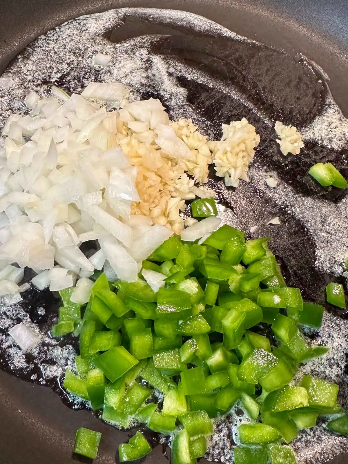A large skillet with melted butter and minced garlic, diced onion, and diced green bell pepper.