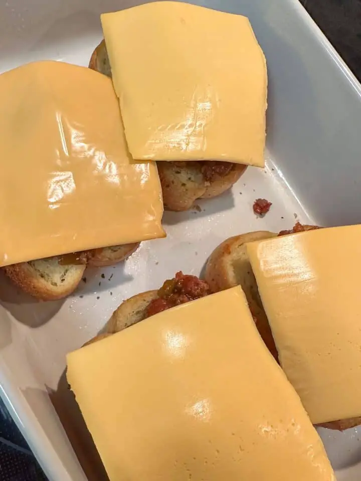 A white casserole dish with pieces of Texas Toast topped with sloppy joe sauce and slices of American cheese that are not melted.