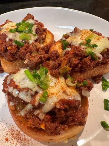 A white dish containing 3 pieces of Texas Toast sloppy joes topped with melted cheddar cheese, green onions, and cayenne pepper.