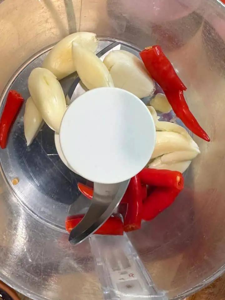 A food processor containing garlic cloves and red chilis.