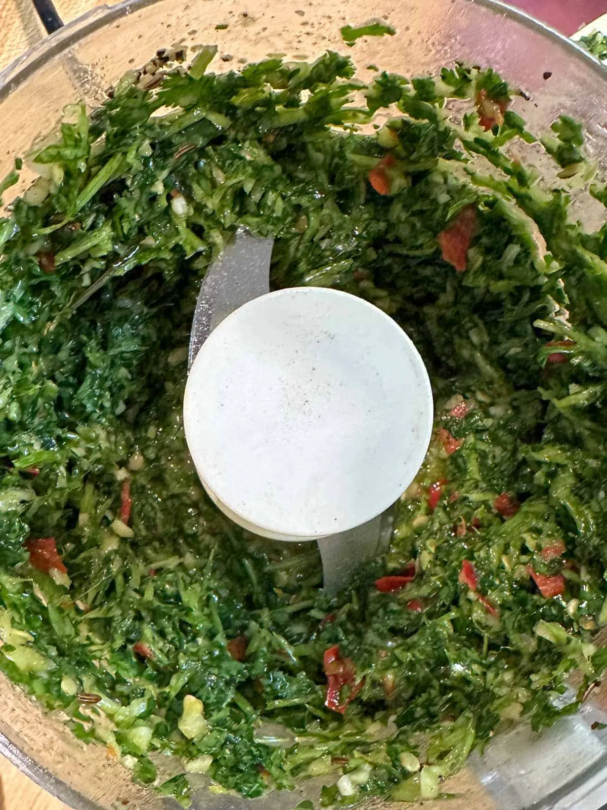 A food processor containing finely chopped cilantro, garlic, and chilis.