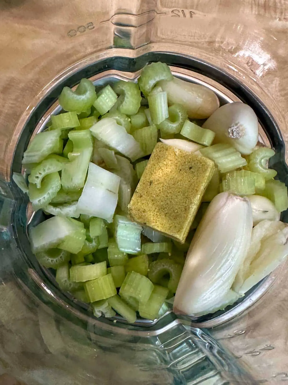 A blender containing garlic, diced celery, and a Maggi Chicken Bouillon Cube.