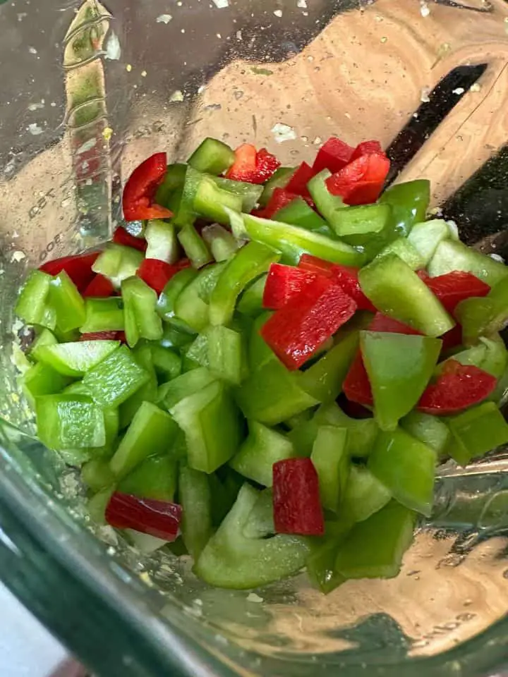A blender containing diced green bell peppers and red bell peppers.