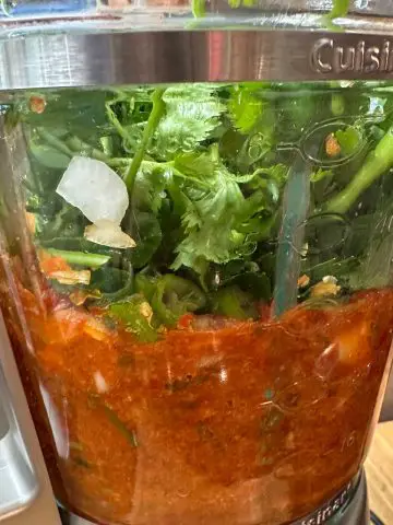 A blender containing blended bell peppers topped with parsley and cilantro.