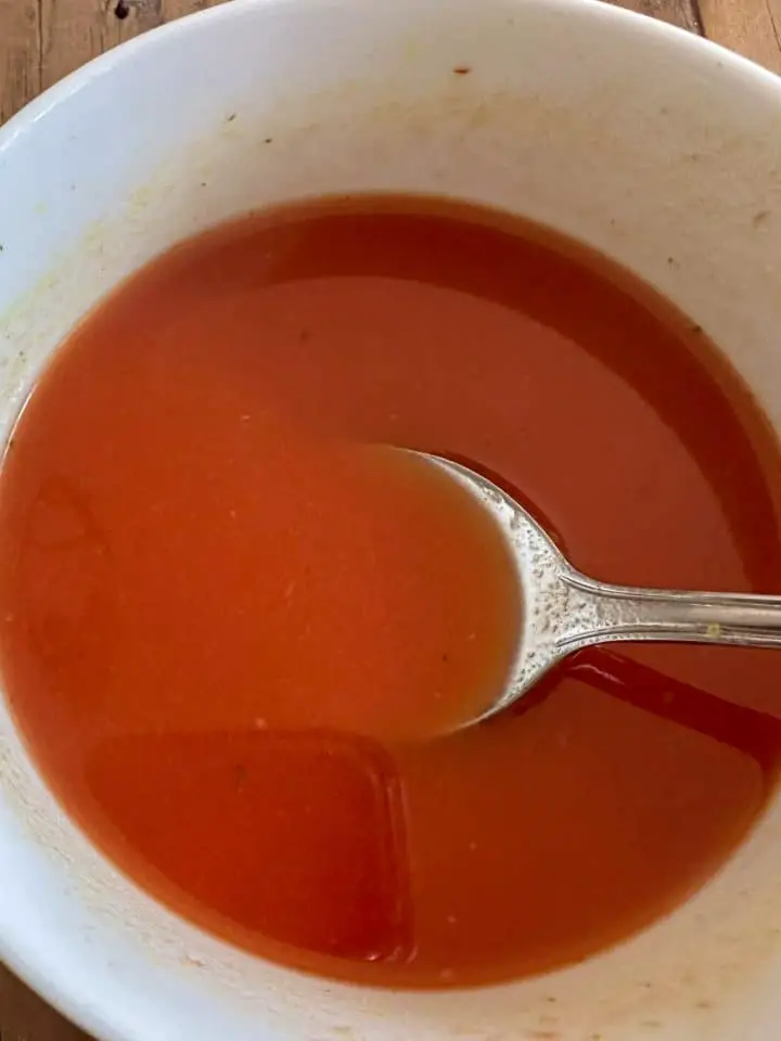 A white bowl containing a tomato sauce with a spoon resting in the bowl.