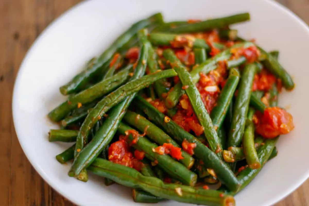 Green beans with tomatoes and garlic in a white bowl.