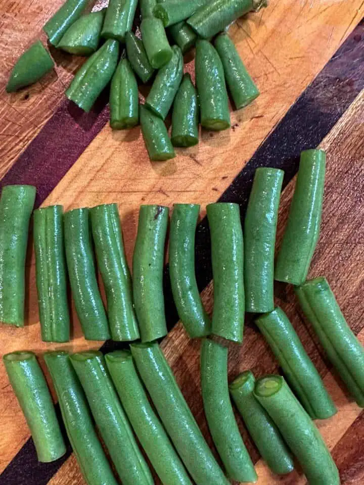 Green beans that have been cut up and topped and tailed on a wooden cutting board.