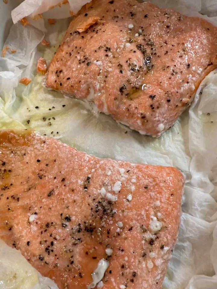 Cooked salmon fillets seasoned with salt and pepper and drizzled with olive oil atop paper towels.