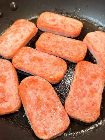 Slices of fried Spam in a large skillet.
