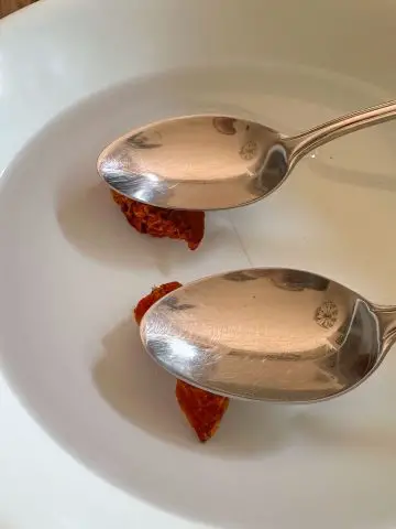 2 dried Ghost chili peppers in water in a bowl with the chilies being held down under the water by spoons.