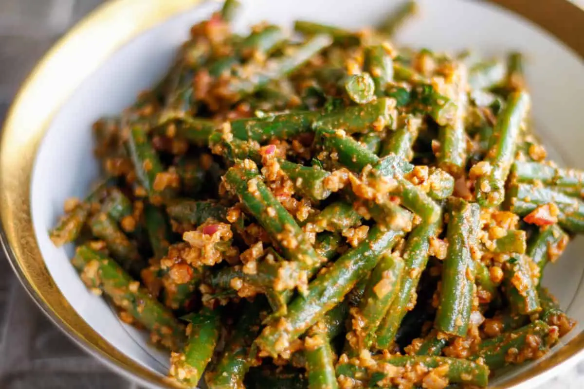 Green beans dressed with a walnut based sauce in a gold rimmed bowl.