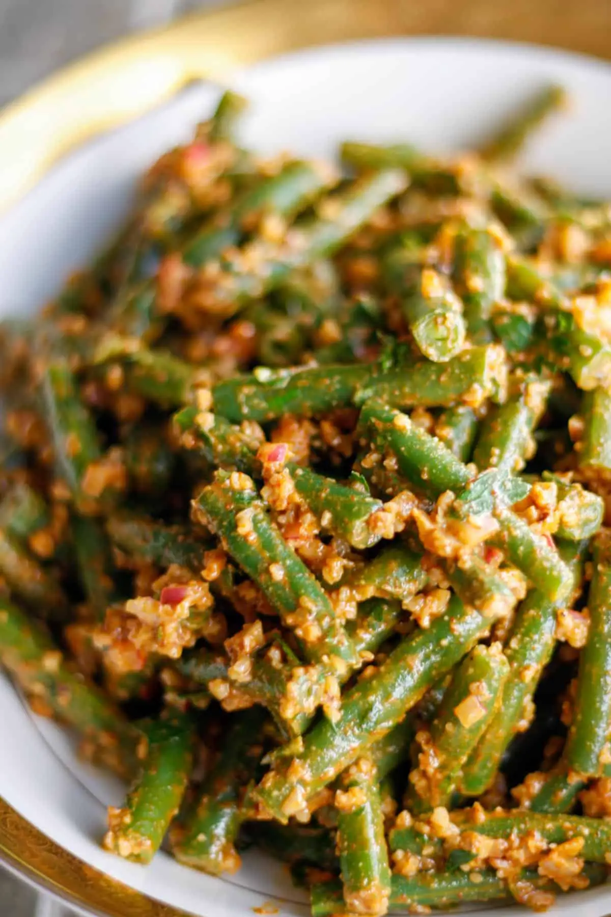 Green beans dressed with a walnut based sauce in a gold rimmed bowl.