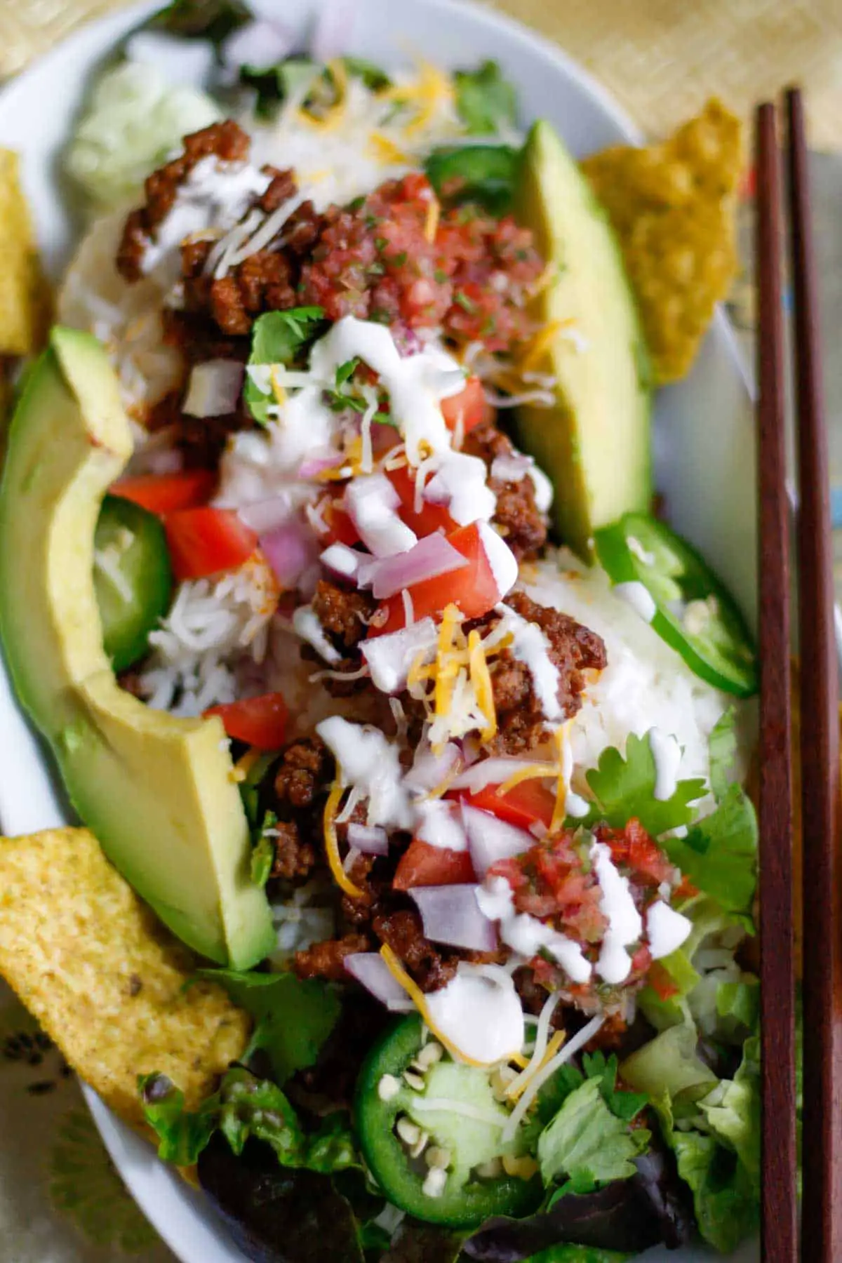 Japanese Taco rice which is rice topped with taco seasoned ground beef garnished with avocado, diced tomato and onion, sliced jalapenos, shredded lettuce and cheese, sour cream and salsa in a white dish.