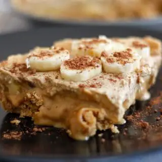 A banoffee pie on a black plate. The pie is topped with banana slices and sprinkled cocoa powder.