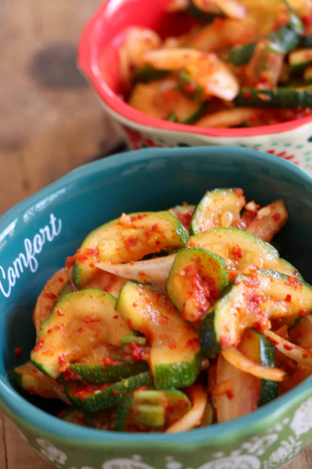 Two bowls containing Korean zucchini kimchi which is kimchi, sliced onions, and green onions in a spicy red sauce.