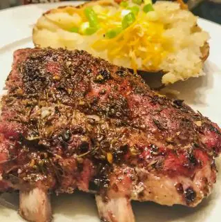 A rack of baby back pork ribs and a baked potato with cheese and green onions on a white plate.