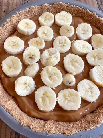 A pie plate containing banoffee pie. You can see the graham cracker crust, toffee filling, and slices of banana.