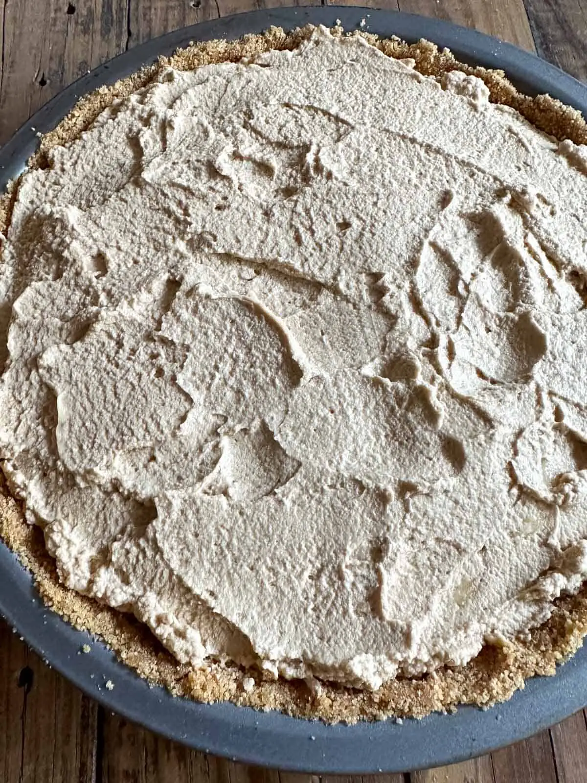 A banoffee pie in a pie pan. You can see the graham cracker crust and whipped cream topping.