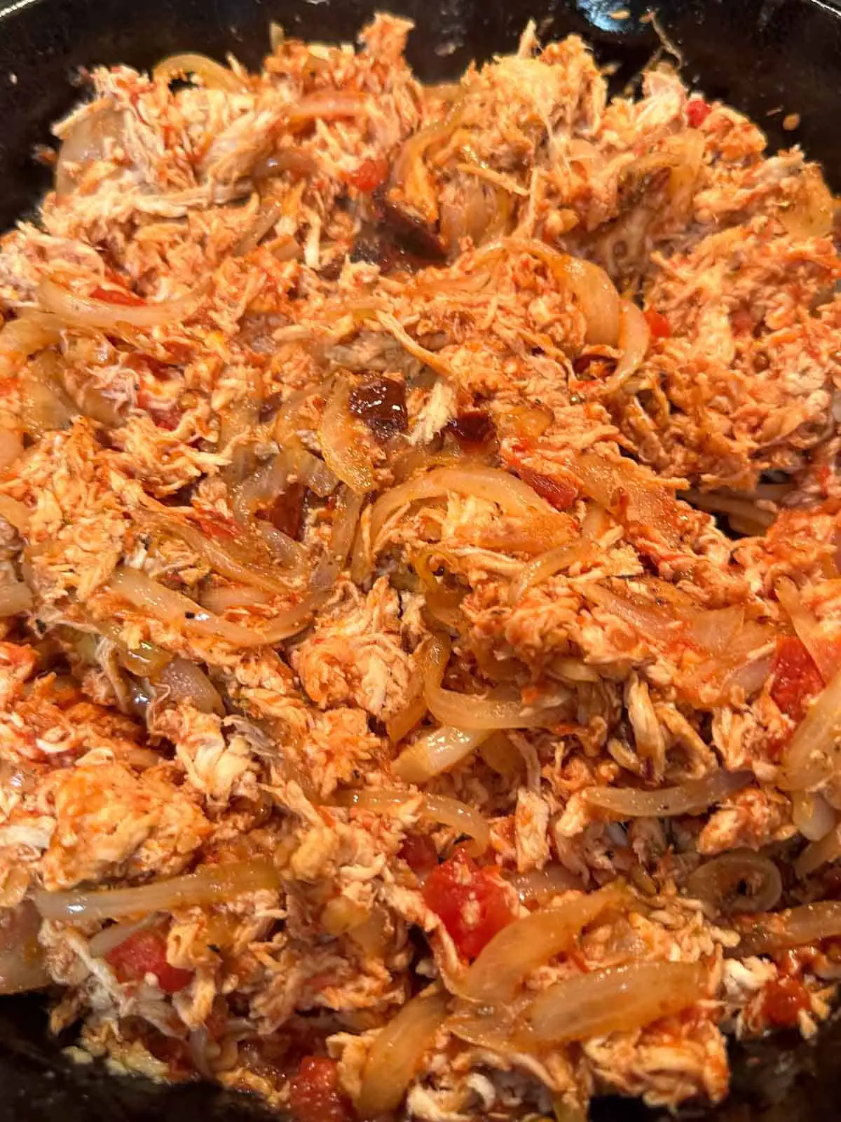 Shredded chicken cooked with tomatoes, onions, and chipotle peppers in an adobo sauce in a cast iron pan.