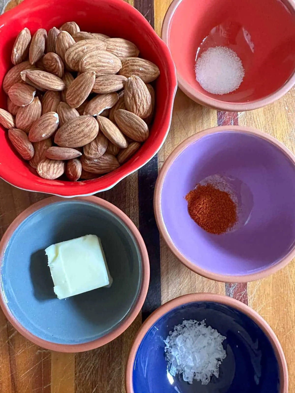 Bowls containing raw almonds, salt, butter, Carolina Reaper powder, and sea salt flakes.