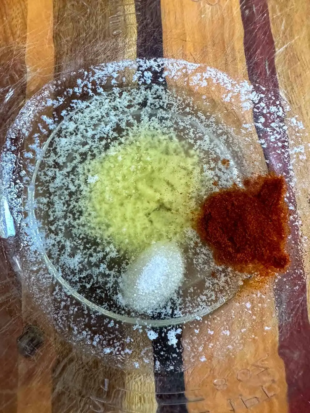 A glass bowl containing melted butter, salt, and Carolina Reaper powder.