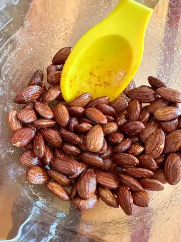 A glass bowl containing Carolina Reaper spicy roasted almonds and a yellow spoon.