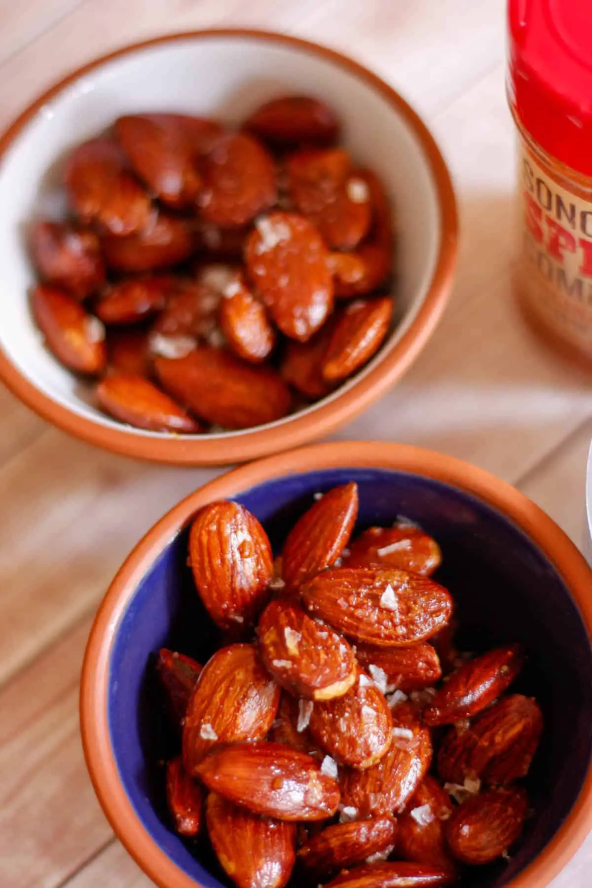 Small bowls filled with roasted almonds garnished with sea salt flakes, and bottle of Carolina Reaper powder on the side.