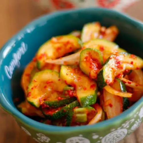 A bowl containing Korean zucchini kimchi which is kimchi, sliced onions, and green onions in a spicy red sauce.