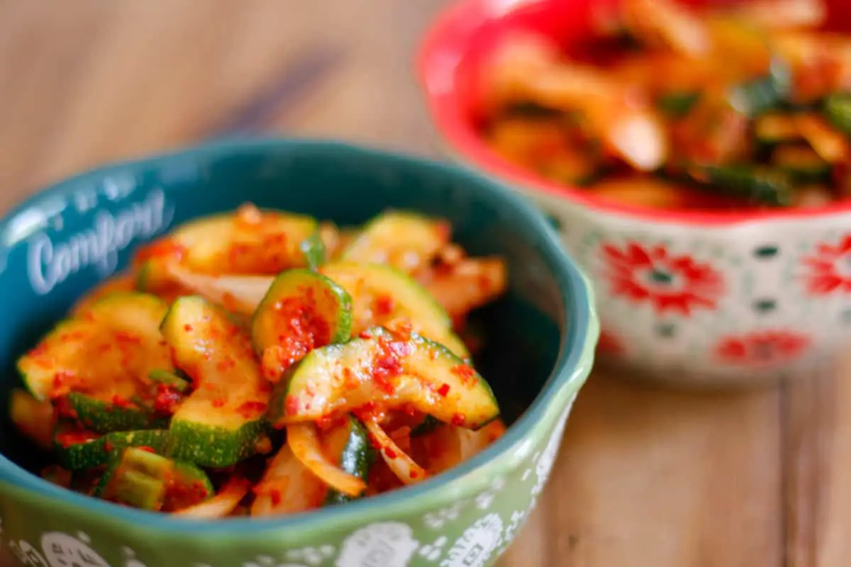 Two bowls containing Korean zucchini kimchi which is kimchi, sliced onions, and green onions in a spicy red sauce.