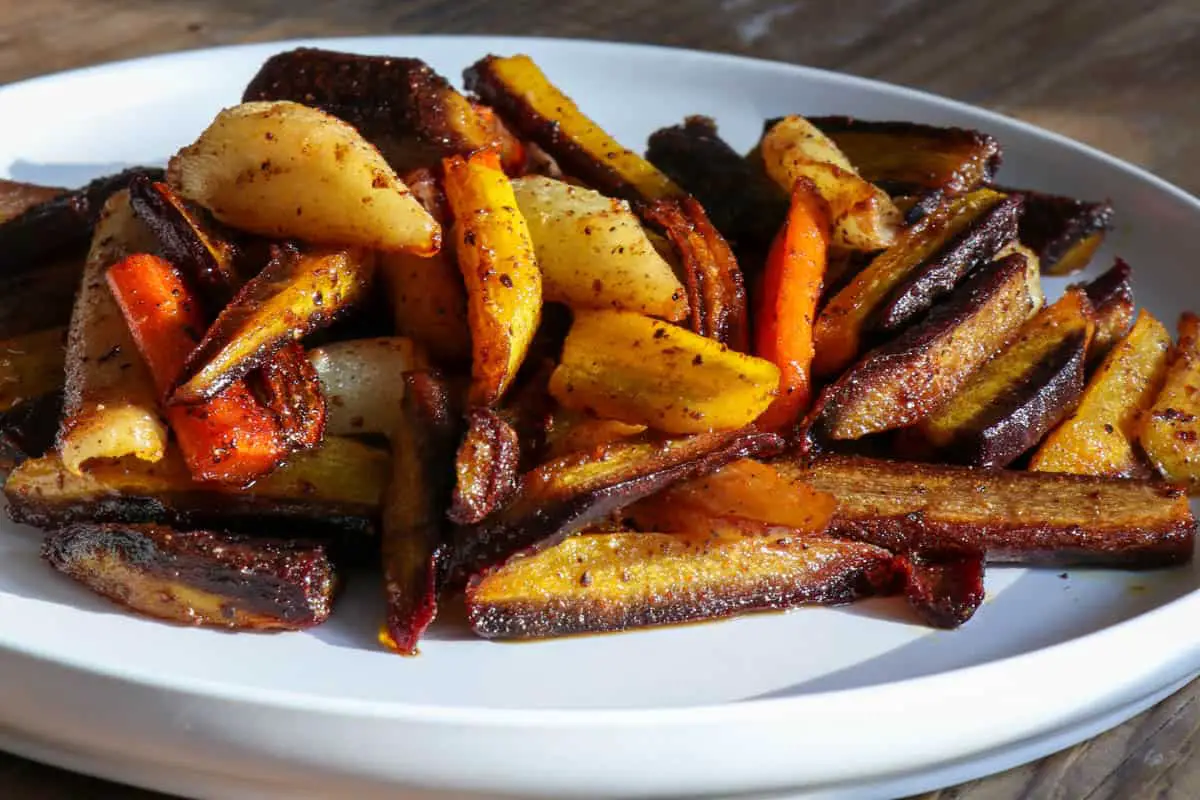 Multicolored carrots cut into slivers and wedges on a white dish.