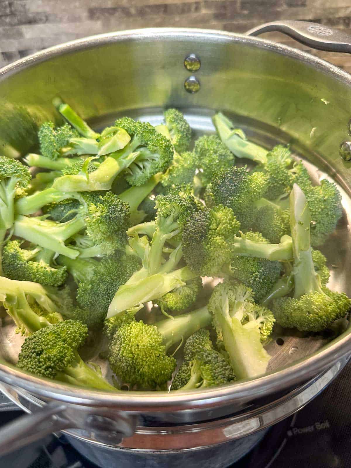 Broccoli florets steaming in a steamer on top of a stove.