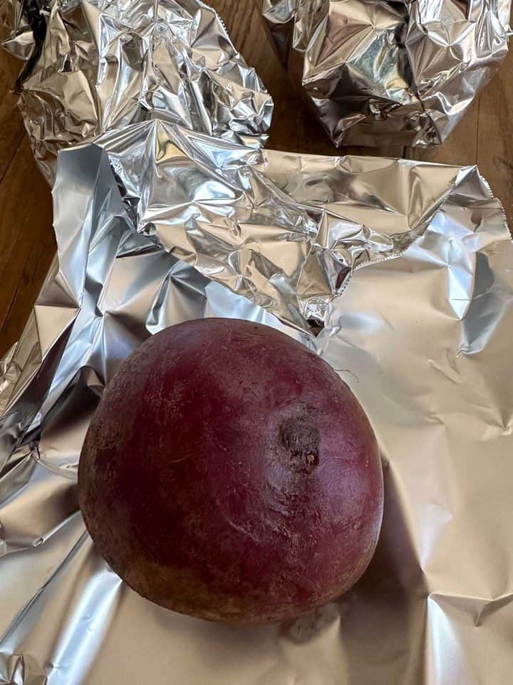 Beets wrapped in foil in the background and a beet placed on top of a sheet of foil.