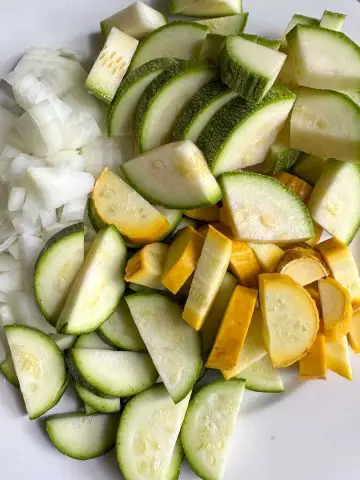 Chopped onion and sliced zucchini both green and yellow on a white plate.