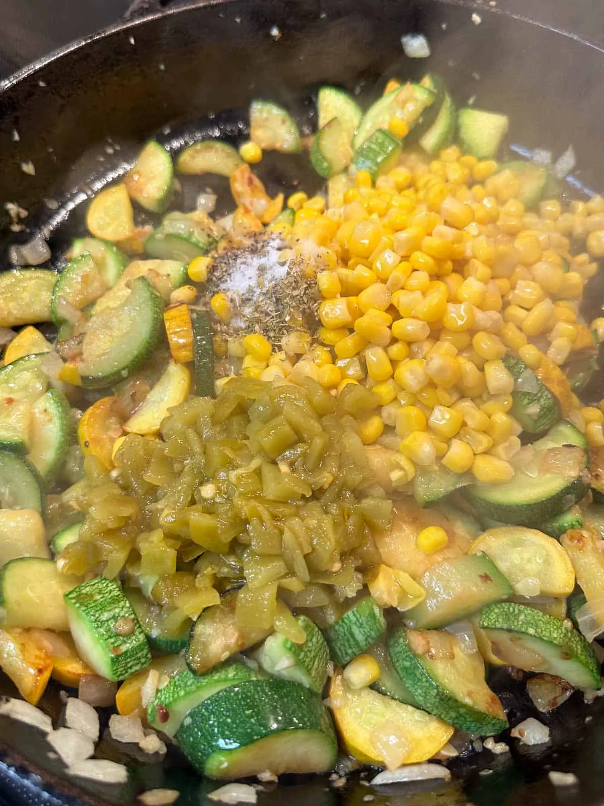 Sliced squash and chopped onion in a cast iron pan topped with green chilies, seasonings, and corn.