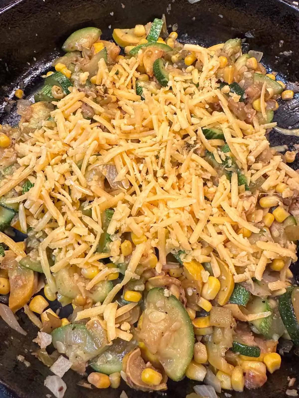 Sliced squash cooked with chopped onion, green chilies and corn covered with shredded cheese in a cast iron pan.