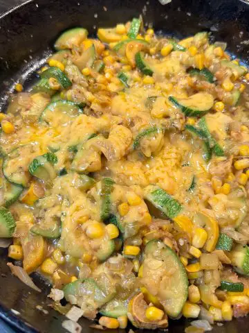 Sliced squash cooked with chopped onion, green chilies and corn covered with melted cheese in a cast iron pan.