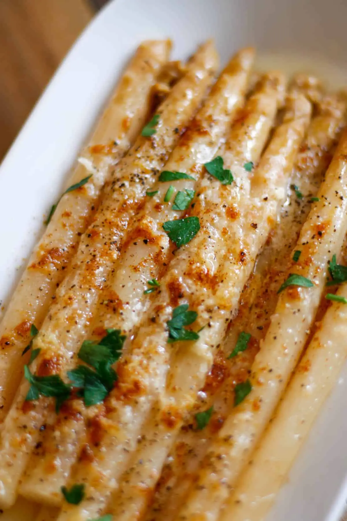 White asparagus spears in a white serving dish with melted Parmesan cheese garnished with Italian parsley.