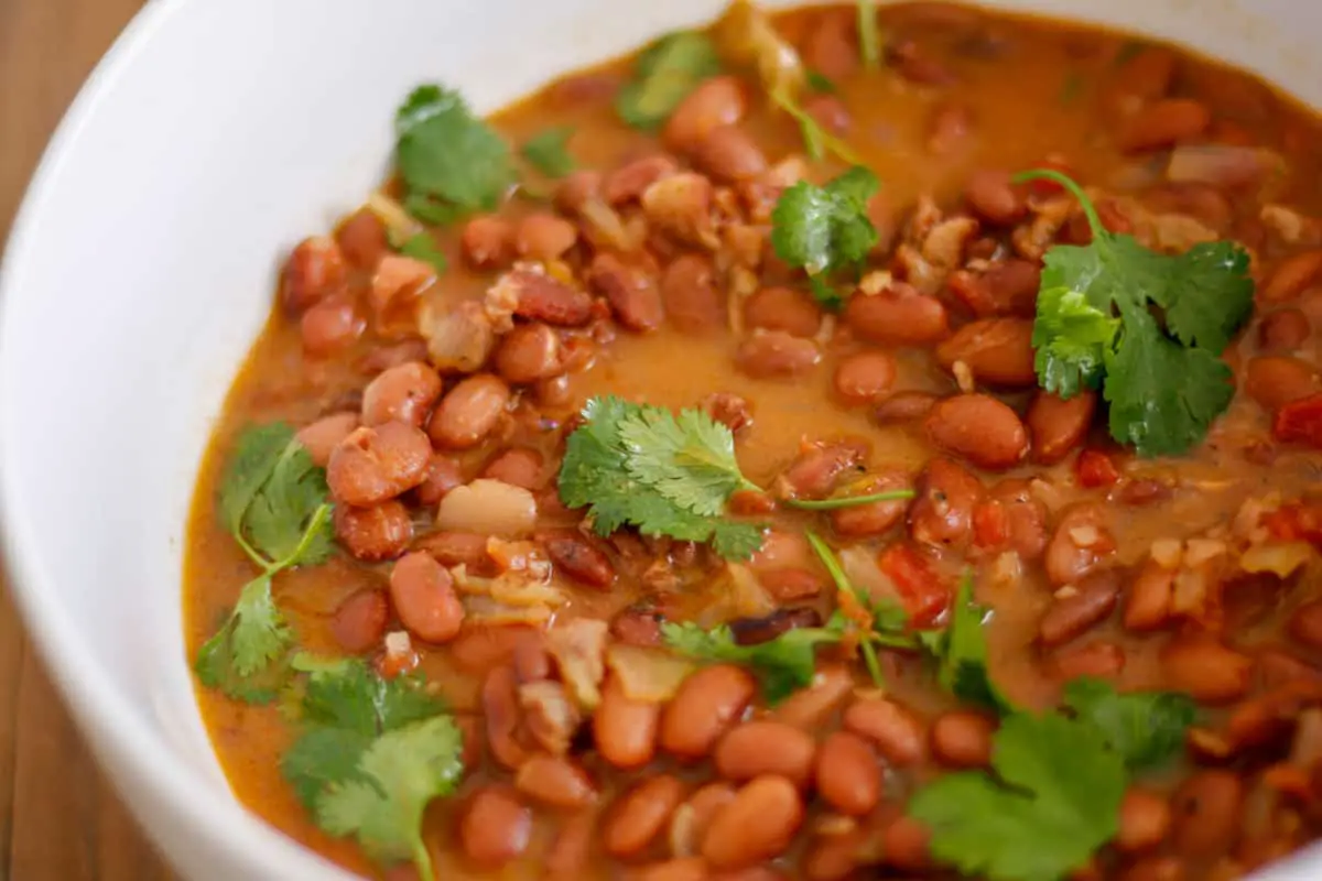 A large white bowl containing borracho beans which is pinto beans in a beer broth garnished with cilantro.