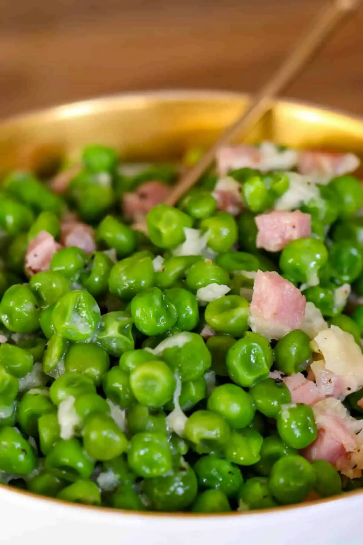Peas, ham and garlic in a gold rimmed dish with a spoon with a gold handle in the peas.
