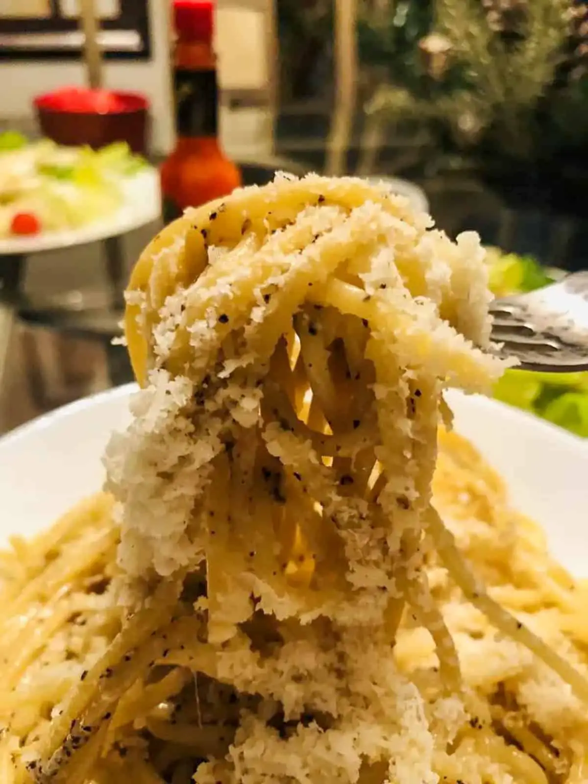 Cacio e pepe with grated pecorino romano cheese being held by a fork. There is a salad in the background.