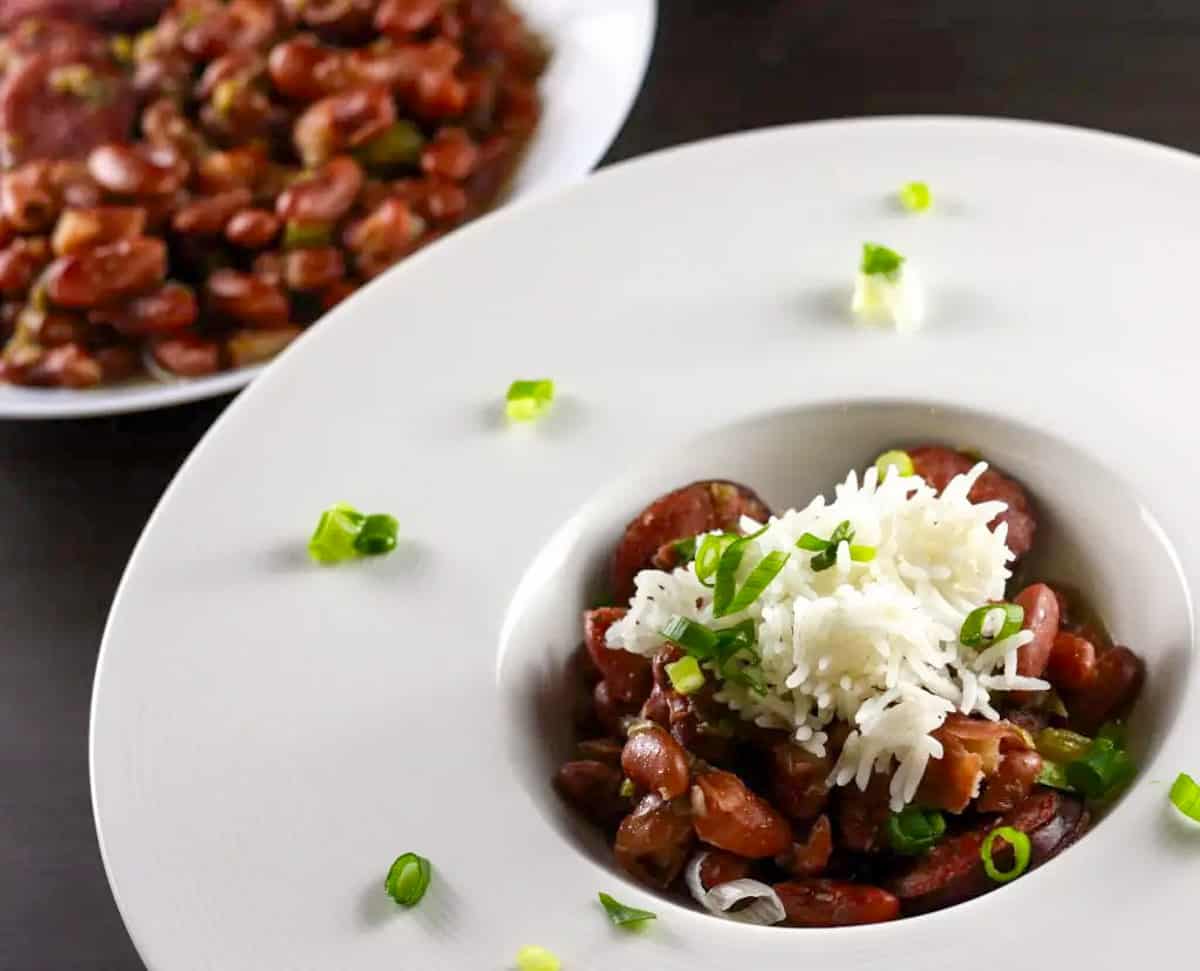 New Orleans Red Beans and Rice in a white bowl, garnished with green onions. There is a bowl of red beans in the background.