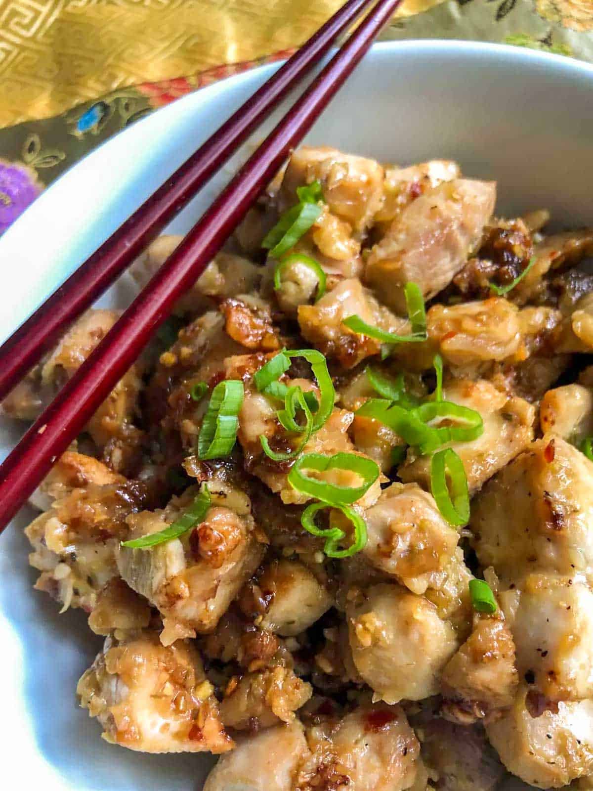 Vietnamese Lemongrass Chicken garnished with green onions in a bowl. There is a pair of chopsticks resting on the side of the bowl.