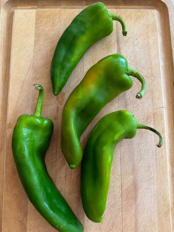 Four Anaheim peppers on a wooden cutting board.